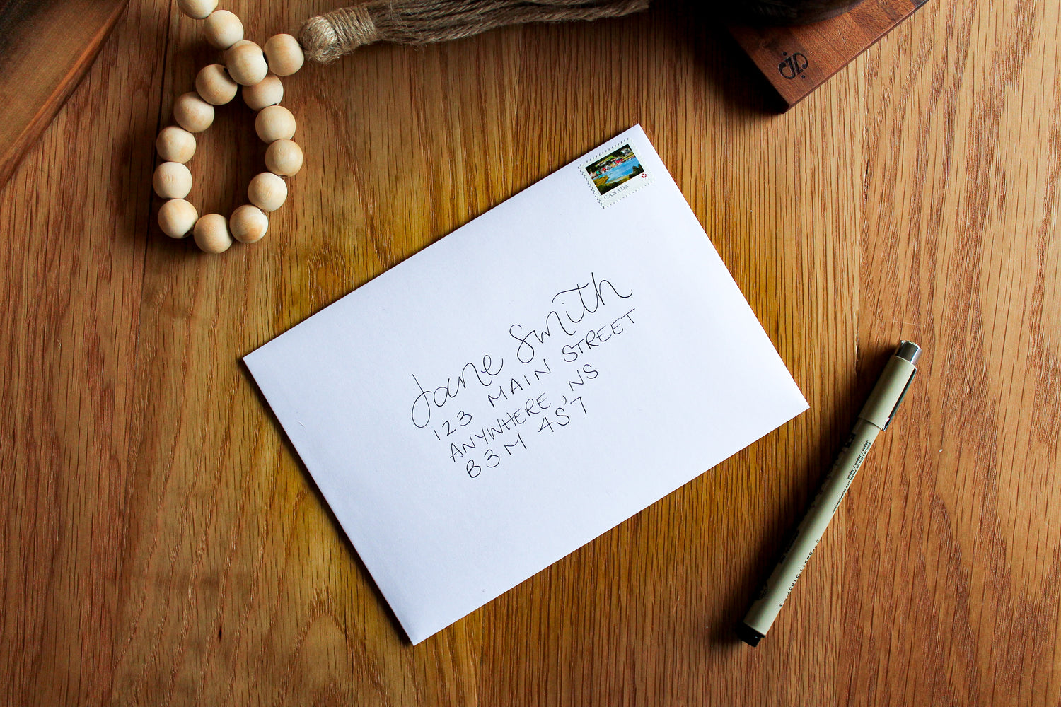 White hand-addressed envelope on a wooden table with a pen beside it.