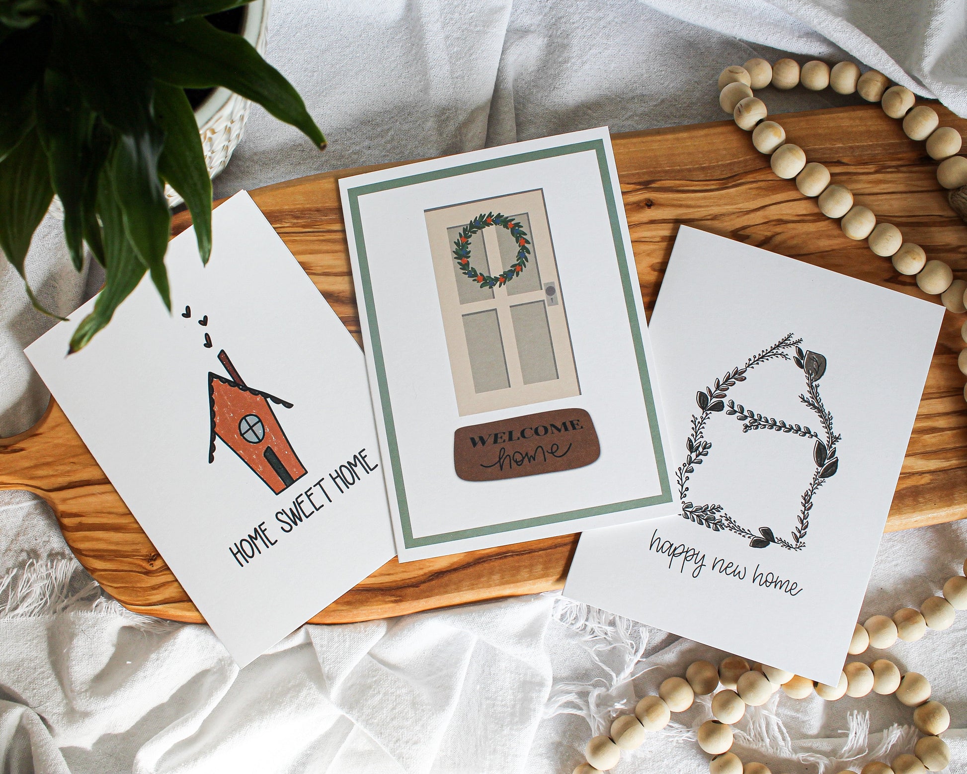 Three new home greeting cards laying flat on a olive wood serving board